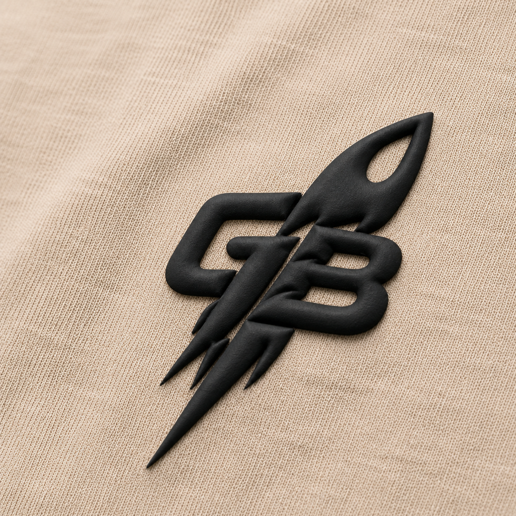 Close-up of the tonal black puff-print GB rocket emblem on the GLXY Orbit 001 Vintage Cream t-shirt