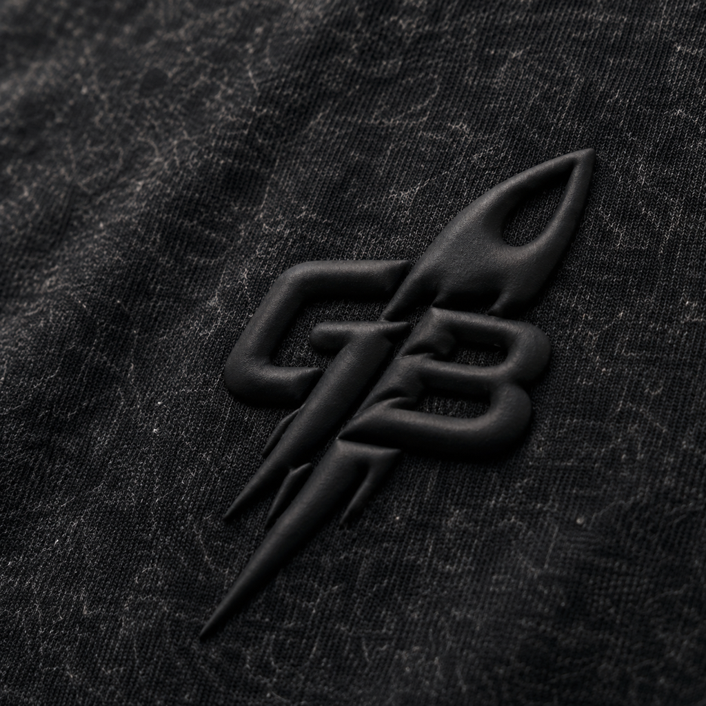 Close-up of the tonal puff-print GB rocket emblem on the GLXY Orbit 001 Vintage Black t-shirt