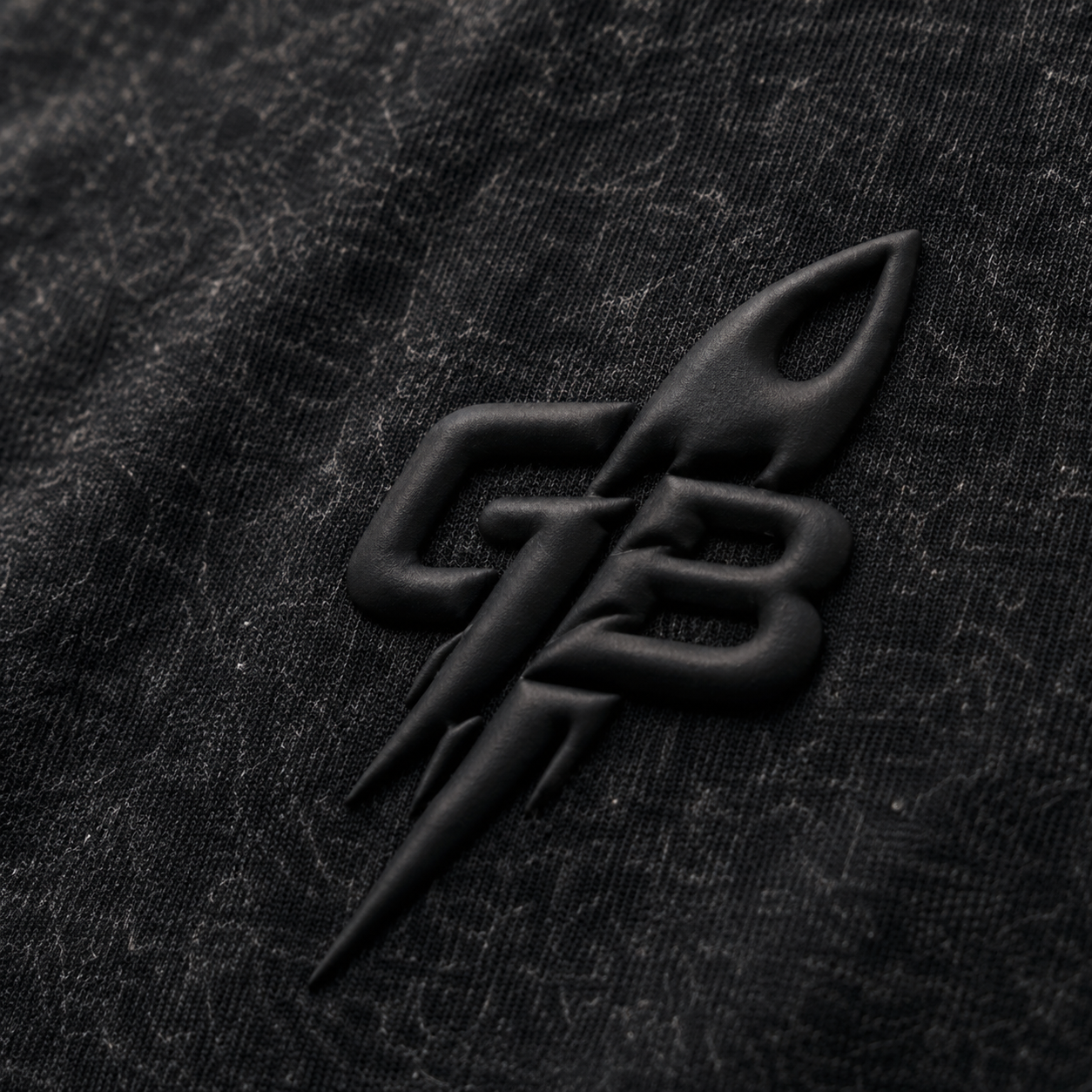 Close-up of the tonal puff-print GB rocket emblem on the GLXY Orbit 001 Vintage Black t-shirt