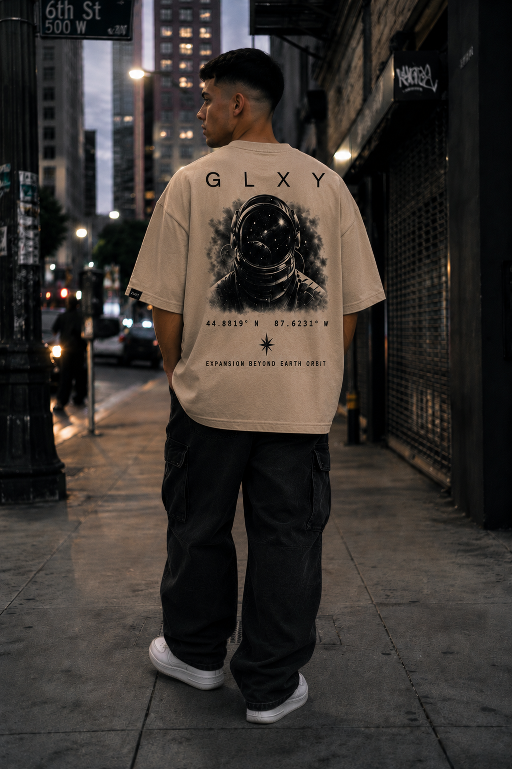 Back view of a street model wearing the GLXY Orbit 001 Vintage Cream t-shirt featuring astronaut artwork